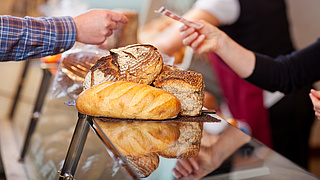 In einer Bäckerei wird eine Auswahl an Brot mit einem Geldschein bezahlt.