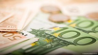 Nahaufnahme von 100-Euro- und 50-Euroscheinen, weiter hinten liegen verschwommen zwei Münzen.