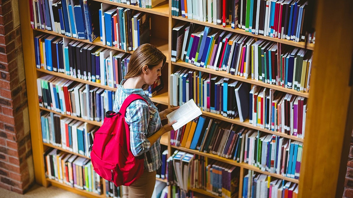 Studentin vor einem Bücherregal in einer Bibliothek.