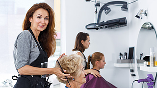 Eine Friseurin im Salon frisiert einer Seniorin die Haare.