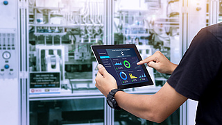 Jemand bedient ein Tablet vor einem durchsichtigen Schrank mit Elektronik.