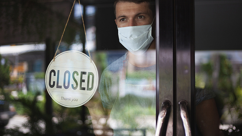 Ein junger Mann steht in einem Restaurant hinter einer Glastür, an der ein "Closed"-Schild hängt.