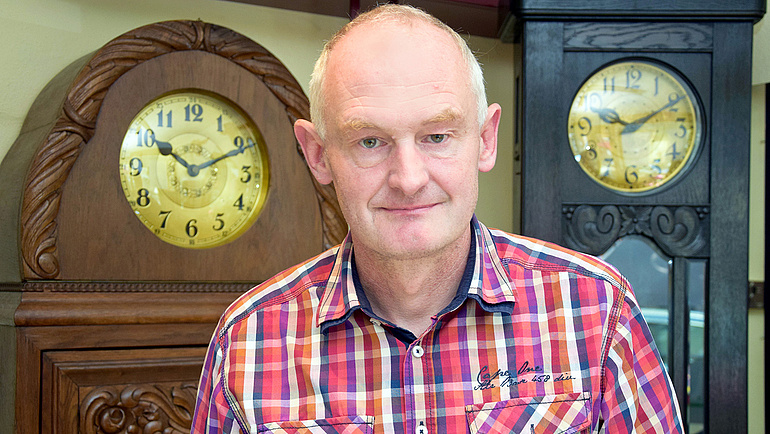 Uhrmacher Carsten Handrick in seinem Laden, im Hintergrund zwei große Standuhren.