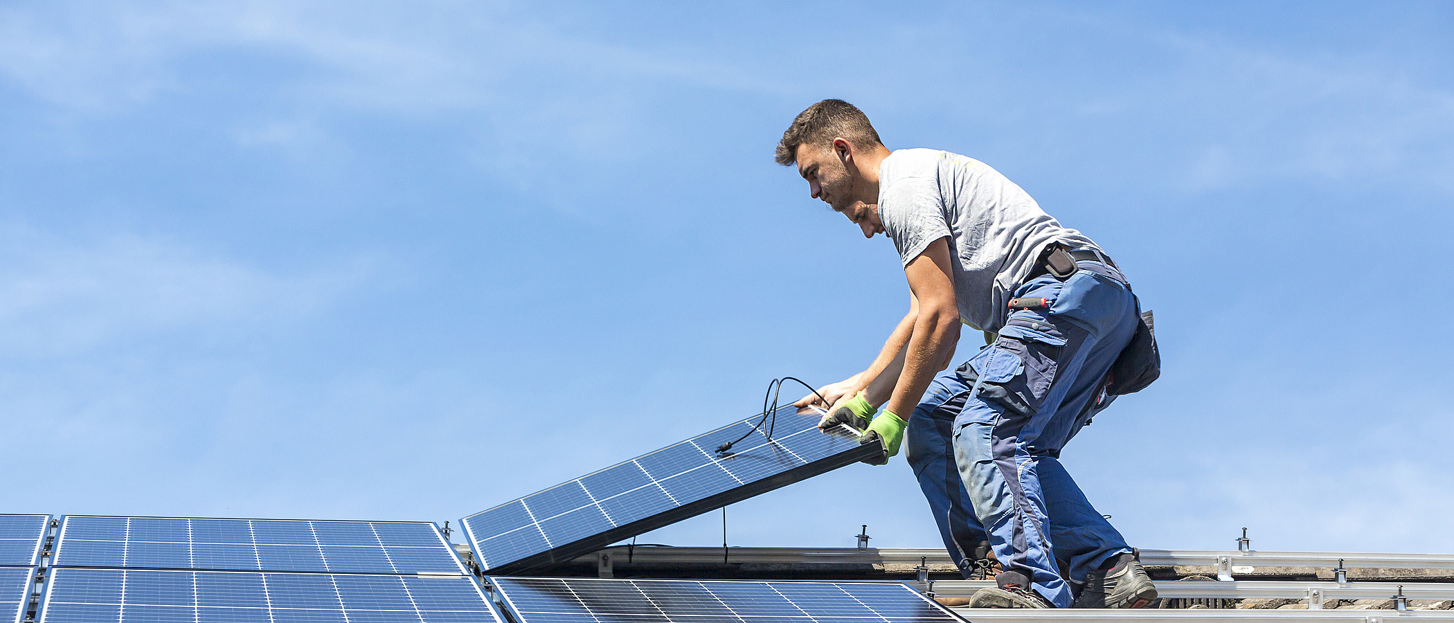 Ein Handwerker installiert Solarpanele auf einem Hausdach.