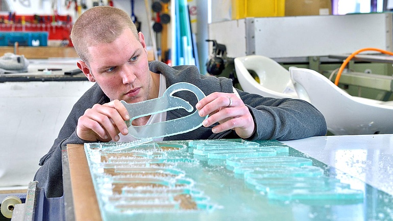 Ein junger Mann betrachtet ausgestanzte Buchstaben aus hellblauem Kunststoff.