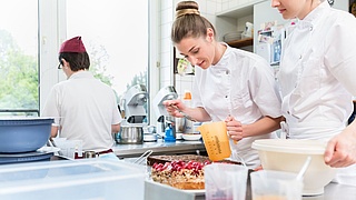 Konditorinen backen einen Kuchen. Eine weitere Person im Hintergrund.