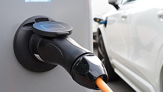 Ein weißes Fahrzeug wird an einer Ladesäule für Elektrofahrzeuge geladen. Im Vordergrund ist der schwarze Stecker zu sehen.