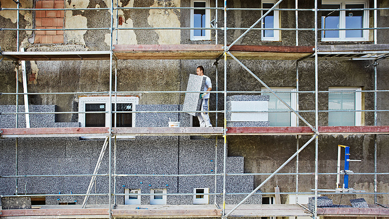 Ein Handwerker bringt Dämmmaterial an einem Gebäude an.