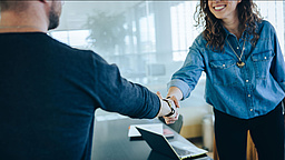 Eine Frau und ein Mann geben sich im Büro die Hand.