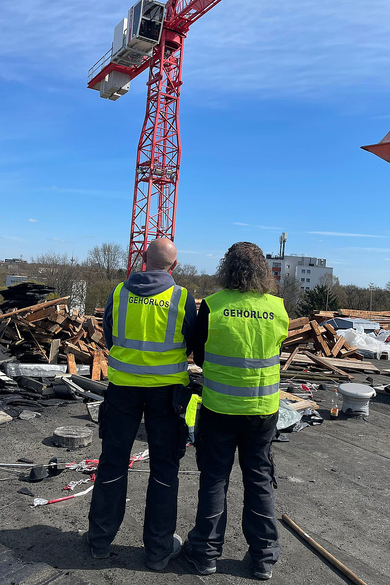 Zwei Mitarbeiter mit Warnwesten und der Aufschritt "Gehörlos" auf der Baustelle.