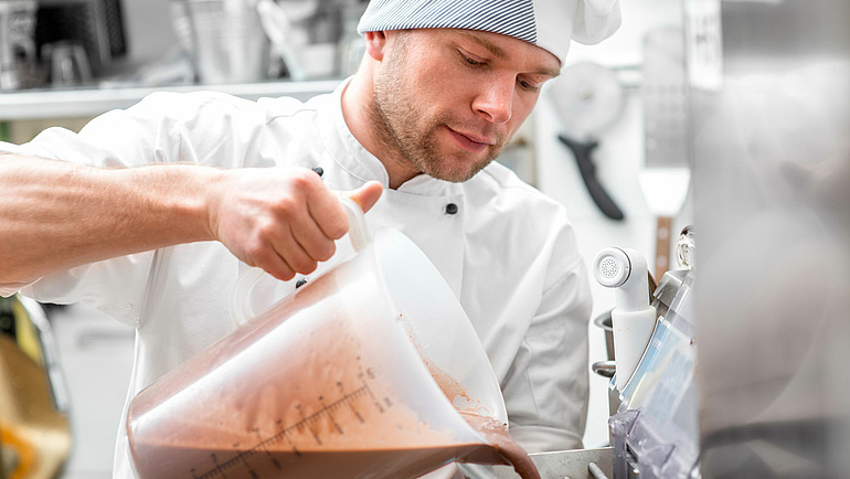 Junger Mann mit an Eismaschine stellt Schokoladeneis her.