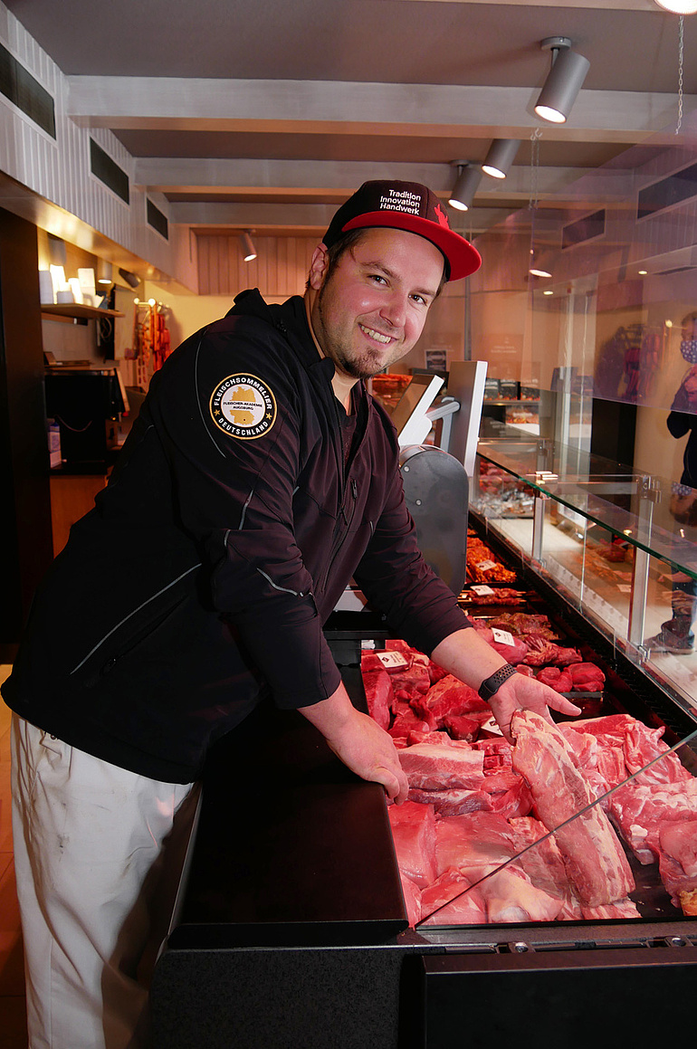 Fleischermeister Lennart Hermstein präsentiert Fleischstücke in einer Verkaufstheke.