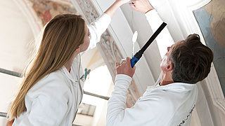 Stuckatkeure untersuchen Verzierungen an einer Kirchendecke.