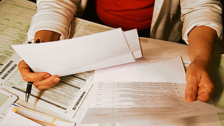 Ausschnitt einer Person, die zahlreiche Unterlagen und Formulare betrachtet.