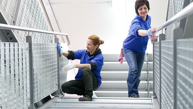 Zwei Damen in blauen Shirts reinigen ein Treppengeländer.