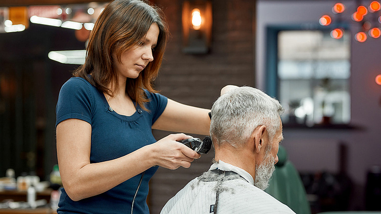 Friseurin in Barbershop rasiert einem grauhaarigen Mann die Haare im Nacken.