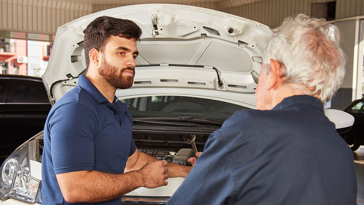 Ein jüngerer und ein älterer Automechaniker vor einer geöffneten Motorhaube.
