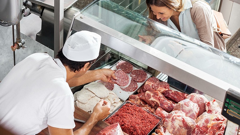 Blick von oben auf eine Fleischertheke: Eine Kundin wird von einem Fleischer bei der Auswahl beraten.