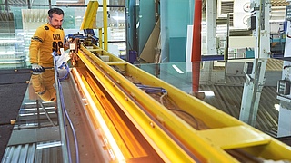 Mann in einer Glaserei schneidet Glasscheibe an einer Schneidemaschine.