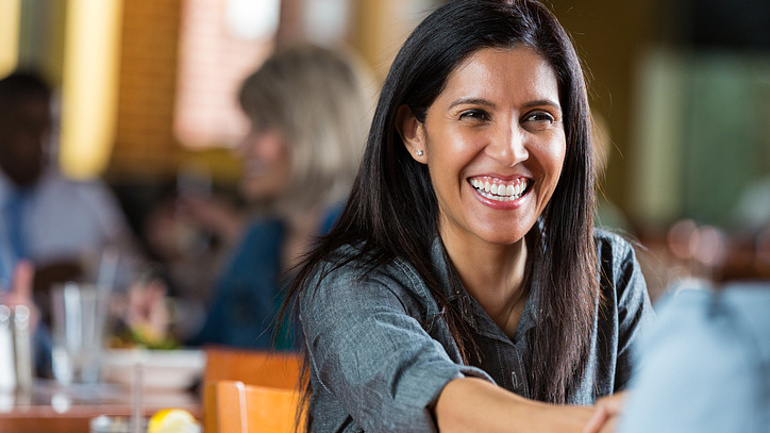 Lächelnde Frau in einem Restaurant gibt ihrem Gegenüber die Hand.