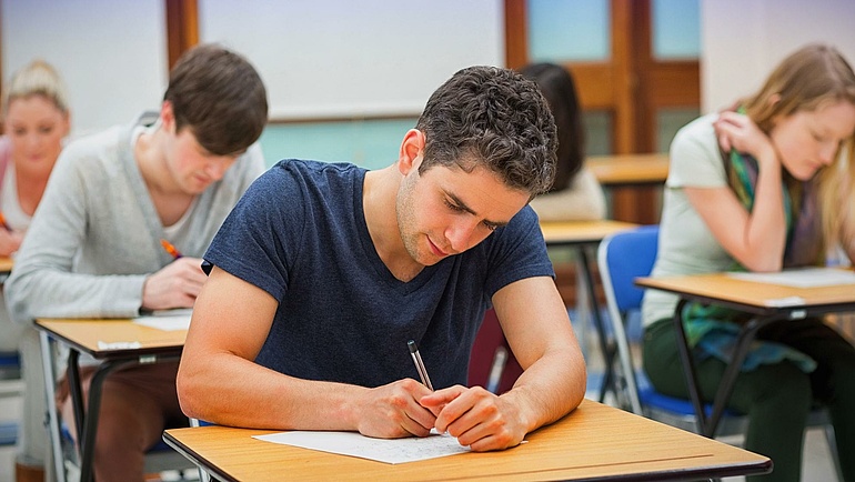 Studenten sitzen einzeln an Tischen und schreiben eine Prüfung.