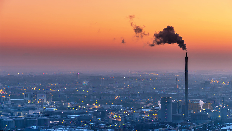 Das Foto zeigt eine Stadt im Dämmerlicht und einen rauchenden Schornstein eines Wärmekraftwerkes.