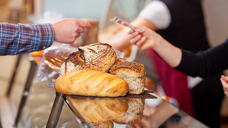 In einer Bäckerei wird eine Auswahl an Brot mit einem Geldschein bezahlt.