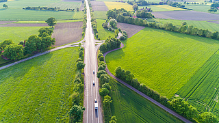 Ein Landstraße in einer grünen Landschaft aus der Vogelperspektive.