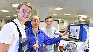 Jugendliche Azubis und Ausbilder an einer Drehmaschine. So sieht moderne Berufsausbildung im Handwerk aus.