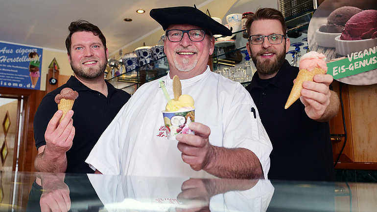 Drei Männer halten Eis (in der Waffel oder im Becher) in die Kamera.