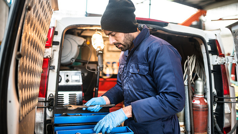 Handwerker im blauen Anzug ordnet Arbeitsgegenstände im Heck eines Lieferwagens.