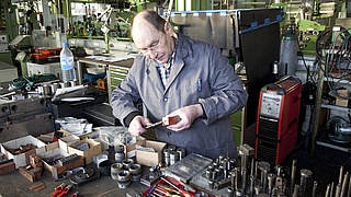 Älterer Handwerker bearbeitet ein Metallstück.