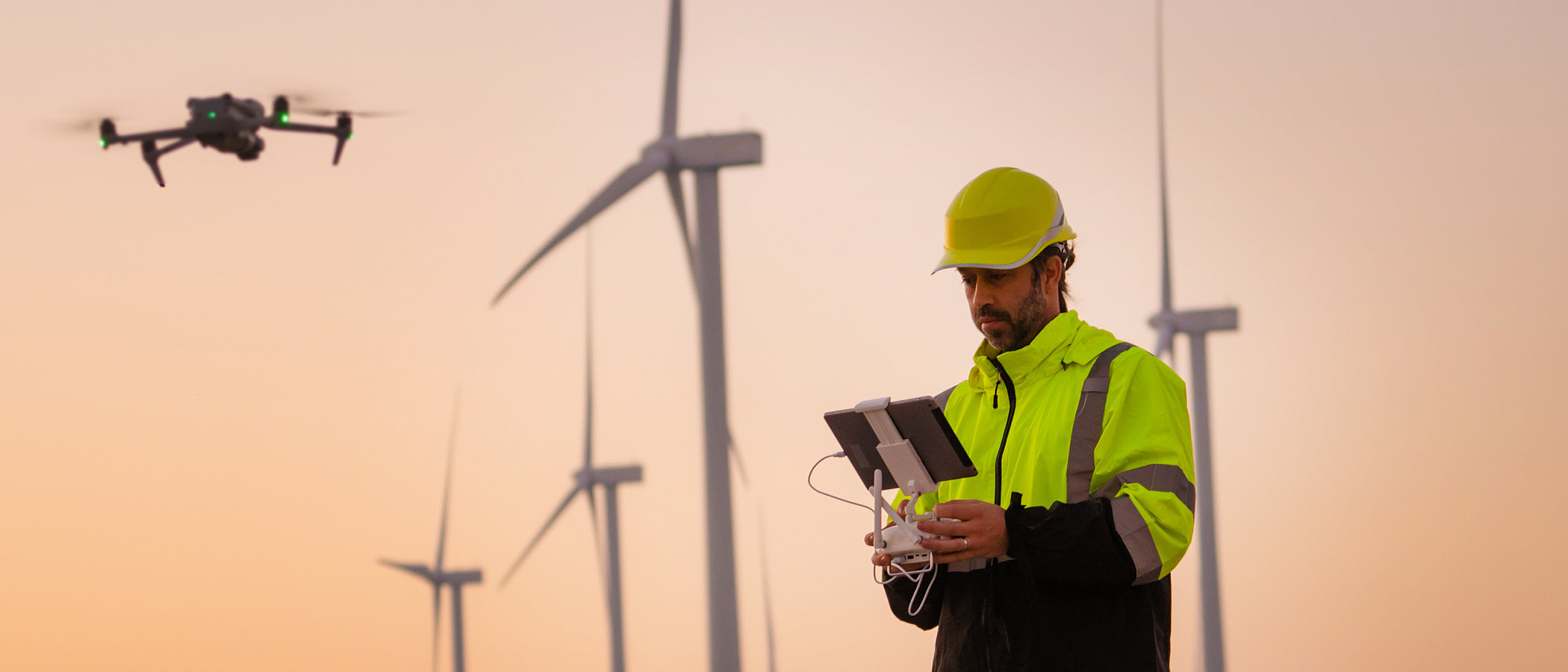 Ingenieure lassen Drohnen fliegen und vermessen und überprüfen Windkraftanlagen während eines Sonnenuntergangs.