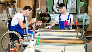 Tischler im Rollstuhl arbeitet an einer Werkbank.