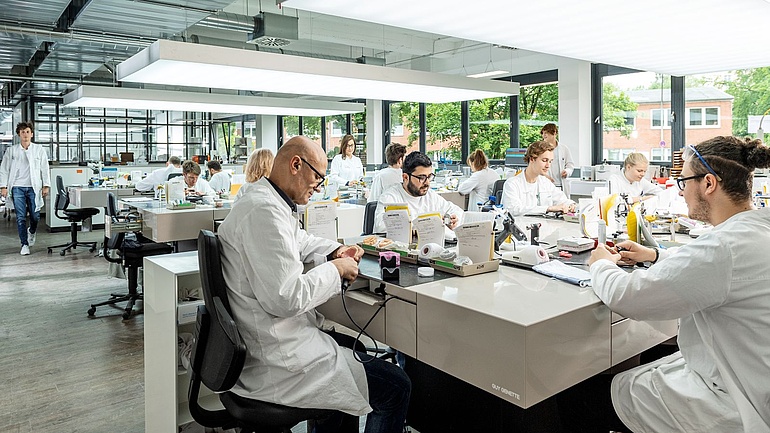 Mitarbeiterinnen und Mitarbeiter arbeiten an Großraumlaborarbeitsplätzen