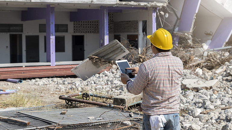 Bauarbeiter mit Bauhelm auf einer Abrissbaustelle mit Tablet.