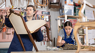 Männliche und weibliche Restauratoren in Arbeitskleidung renovieren antike Stuhlspiegelrahmen in der Reparaturwerkstatt