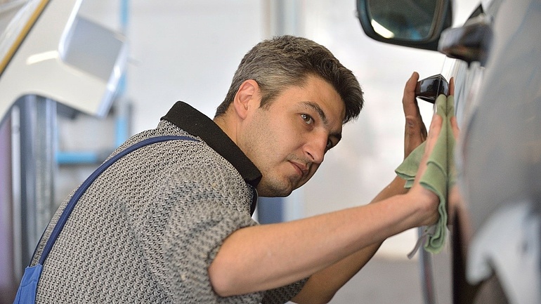 Ein Karosserie- und Fahrzeubaumeister poliert die Karosserie eines Fahrzeugs.