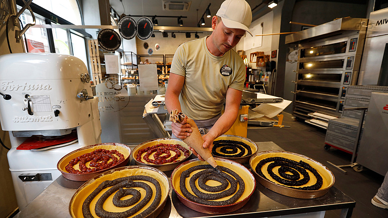 Ein Bäckereimitarbeiter spritzt Brezelteig in verschiedene Formen.