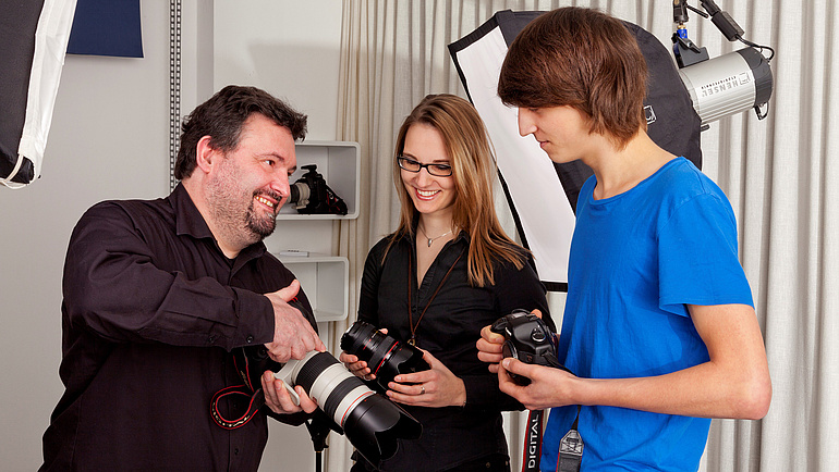 Fotografenmeister erläutert seinen Auszubildenenden die Fotokamera.