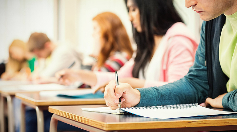 Ältere Schüler sitzen in der Klasse am Tisch und schreiben konzentriert