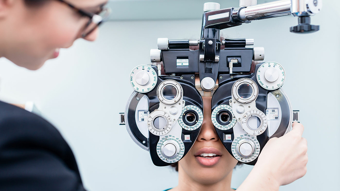 Junge Frau hinter einem Augenmessgerät beim Augenoptiker.
