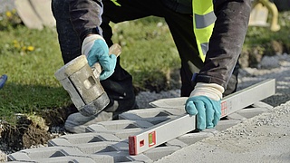Ein Straßenbauer verlegt Bodenplatten am Straßenrand im Übergang zu einer Grünfläche.