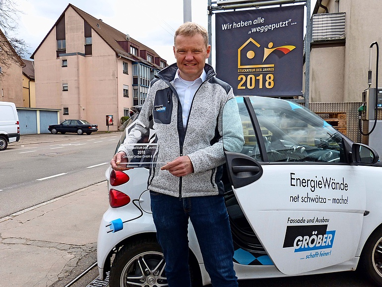 Foto von Christian Gröber mit der Trophäe des Ausbildungspreises der Handwerkskammer Region Stuttgart vor dem Preis-Gewinn, einem Firmen-E-Auto.