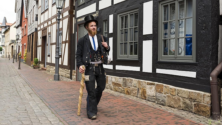 Junger Zimmermann auf der Walz läuft an einem Fachwerkhaus vorbei.