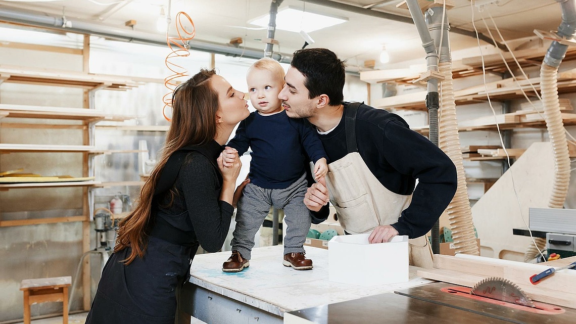 Junges Paar mit kleinem Kind in einer Tischlerwerkstatt.