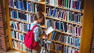 Studentin vor einem Bücherregal in einer Bibliothek.