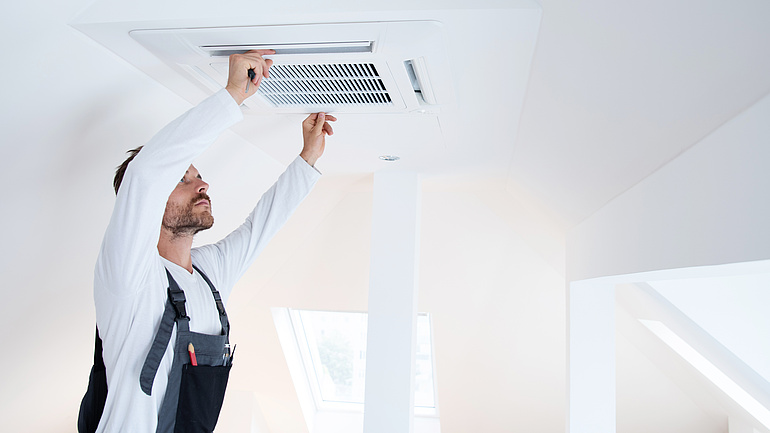 Ein Klimaanlagentechniker birngt die Abdeckung einer Klimaanlage an einer Decke an.