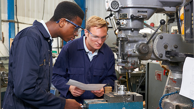 Ingenieur zeugt einem Auszubildenden die Funktionsweise einer Fräsmaschine 