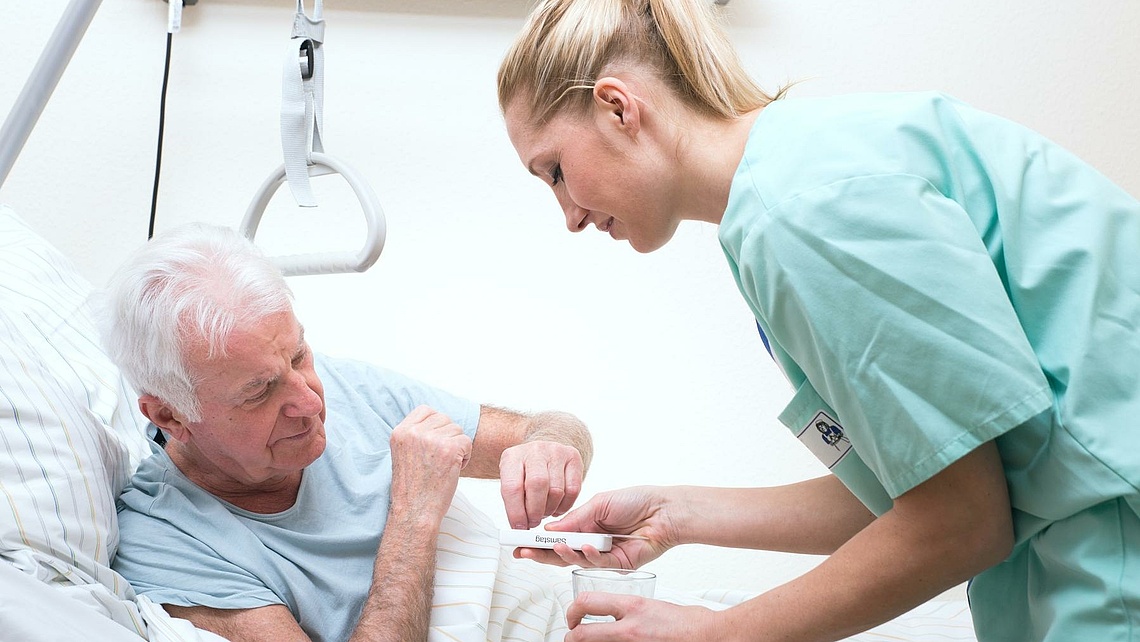 Krankenschwester reicht einem Mann im Krankenhausbett Tabletten.